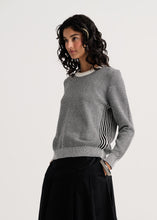 Load image into Gallery viewer, A woman modeling a gray textured knit sweater with black and white vertical striped side panels, paired with a black skirt, against a plain light gray studio background.
