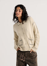 Load image into Gallery viewer, A woman wearing a cream-colored knit cardigan with decorative black dotted stitching details and brown leopard-print pants, photographed against a solid light gray background.
